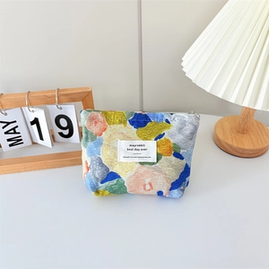 Detail of floral canvas makeup bag with zipper closure and woven label on cream background