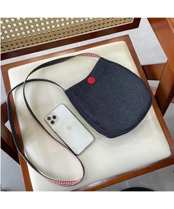 Close-up of denim crossbody bag with red button detail and plaid strap on a chair