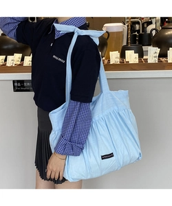 Detail of light blue pleated fabric tote bag featuring decorative bow and Romance label