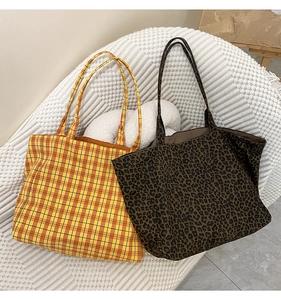 Detail of plaid and leopard print canvas tote bags on a white textured sofa