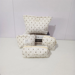 Detailed set of four white quilted cosmetic bags with brown heart patterns and zipper