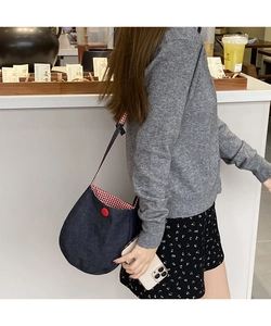 Detail of denim crossbody bag showing red checkered lining and decorative button