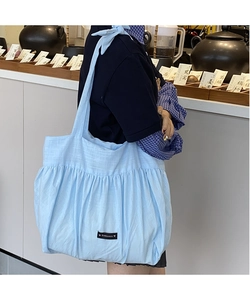 Detail of light blue pleated tote bag showing fabric texture and black woven brand label