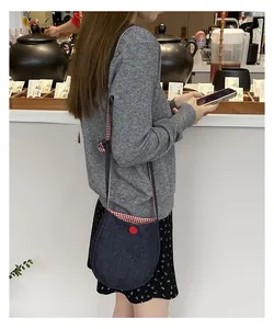 Close-up of a blue denim crossbody bag with a red button and stylish checkered trim detail