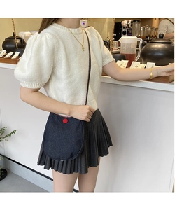 Detail view of a denim saddle bag with red button clasp and thin black shoulder strap