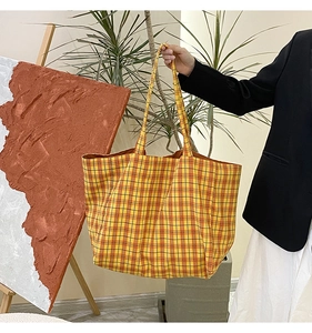 Detail of a large yellow plaid canvas tote bag carried by a model in a casual studio setting