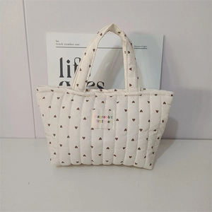 Close-up of white quilted tote bag with brown heart prints and woven logo label