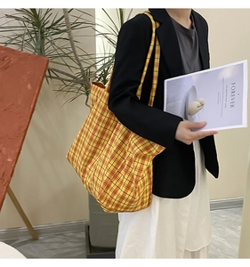 Detail of a large capacity yellow plaid canvas tote bag with woven shoulder straps