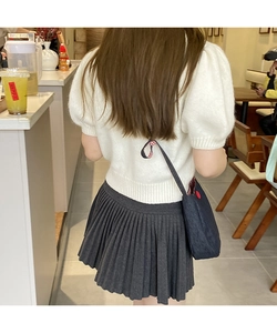Detail of a blue denim crossbody bag paired with a pleated skirt in a cafe setting