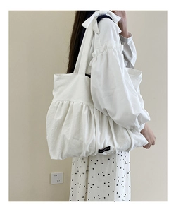 Detail showing white canvas tote bag with layered ruffle design and brand label
