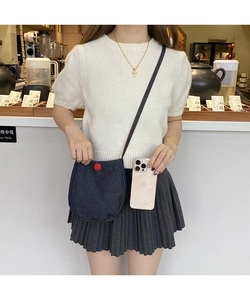 Detail of blue denim crossbody bag with red button decoration and slim strap on model
