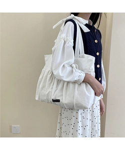 Close-up of white ruffled cotton tote bag featuring a black Romance letter woven label