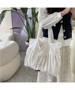 Detail of the white pleated canvas tote bag featuring a minimalist black textile label