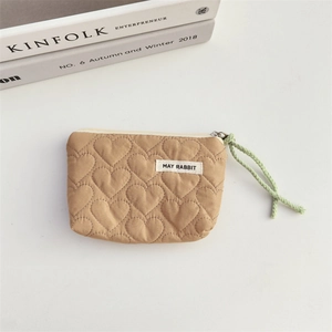 Close-up of heart-quilted light brown mini storage bag with green woven handle and zipper