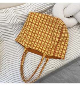 Detail of yellow and orange plaid canvas tote bag with slim handles and brown lining