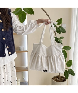 Detail of white cotton linen tote bag featuring pleated texture and tied ribbon shoulder strap