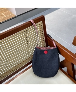 Detail of blue denim shoulder bag with red button and red checkered strap on a wooden chair