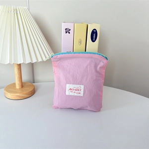 Pink nylon cosmetic pouch with blue zipper and brand label on a minimalist desk