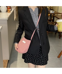 Detail view of red and white plaid crossbody bag worn by model in a casual cafe setting