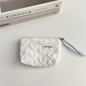 Detail view of white quilted heart pattern pouch with a woven puller on a clean background