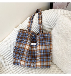 Détail du sac cabas en laine à carreaux avec bouton cœur bleu et étiquette de marque