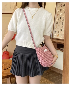 Detail of red and white gingham crossbody bag shown on a model with white knit top
