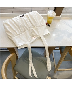 Close-up of white pleated cotton tote bag with minimalist logo tag and fabric strap