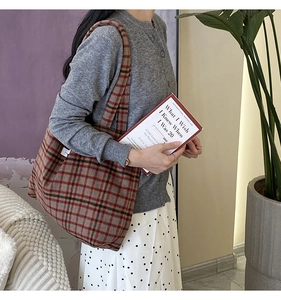 Sac cabas en toile de laine à carreaux rouge et marron porté par un mannequin en intérieur