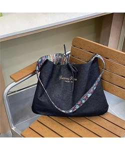 Close-up of black denim tote with yellow embroidery and ethnic geometric pattern strap