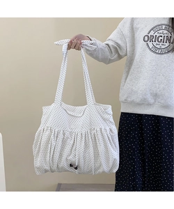 Detail of white polka dot tote bag featuring ruffled bottom and decorative bow handle