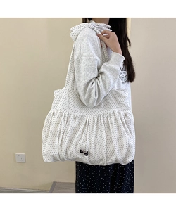 Detail of white tote bag with black polka dots featuring pleated design and thin straps