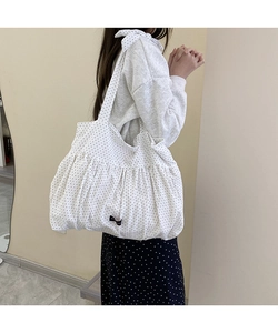 Close-up of white polka dot tote bag with bottom pleats and bow shoulder strap detail