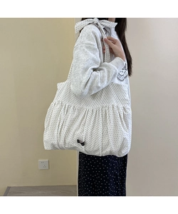 Detail of white polka dot cotton tote bag featuring pleated ruffle trim and bow shoulder strap
