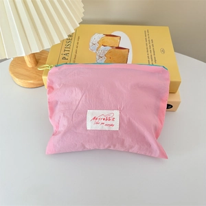 Pink nylon mini makeup bag with green zipper and woven label on a desk with decor
