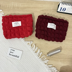 Detail showing red bubble waffle texture canvas makeup bags on a wooden background