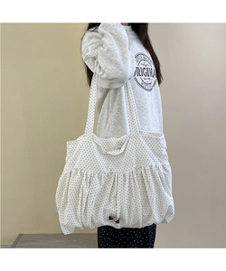 Detail of white tote bag with black polka dots featuring unique pleated design and long strap