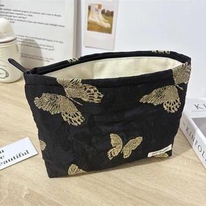 Detail of black canvas makeup bag featuring golden butterfly embroidery and interior lining