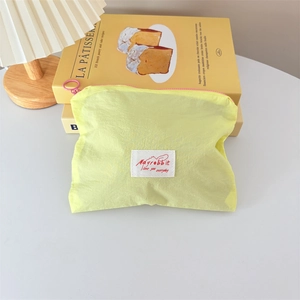 Close-up of yellow fabric cosmetic bag with red brand label and pink ring zipper handle