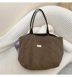 Detail of dark brown canvas tote bag featuring leopard print handles and outer pocket