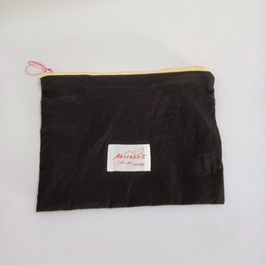 Close-up of black nylon cosmetic pouch featuring a contrast pink zipper and logo patch