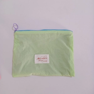 Flat lay detail of a light green nylon makeup pouch with colorful zipper and brand label