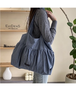 Detail view of a pleated grey-blue cotton linen tote bag with black logo patch