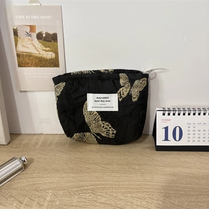 Close-up of black satin makeup bag with golden butterfly embroidery and metal ring zipper