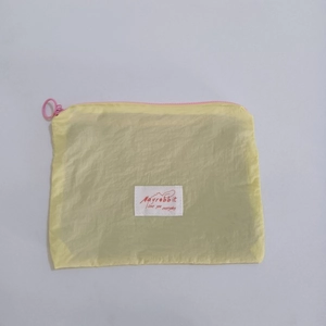 Close-up of yellow nylon cosmetic bag with pink zipper and stitched logo patch