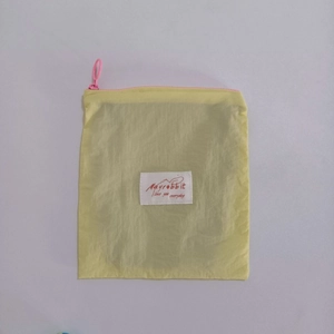 Detail of light yellow pouch with pink ring zipper and white branded woven label