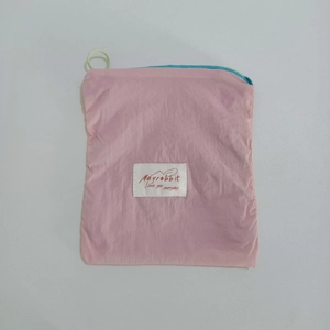 Pink nylon mini storage pouch with top handle and woven label on a gray background