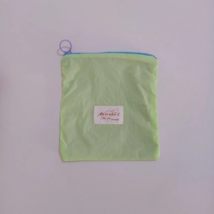 Close-up of green nylon mini storage pouch with purple zipper pull and white brand label