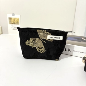 Detail of black jacquard makeup bag featuring a golden butterfly pattern and metal zipper