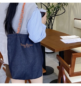 Dettaglio borsa tote in denim blu con tracolla intrecciata arancione e ricamo chic