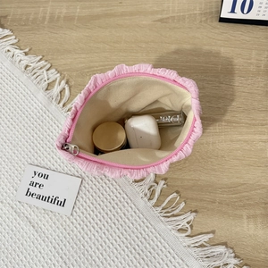 Pink pleated canvas cosmetic bag showing storage space for makeup and earphones